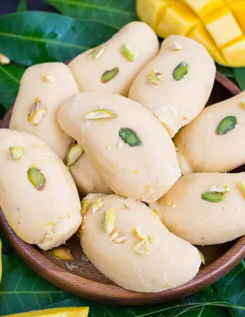 Mango-flavored Indian sweet garnished with pistachios on a wooden plate