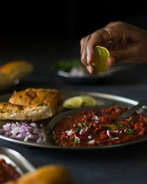 Hand squeezing lemon over spicy Indian curry with bread and chopped onions
