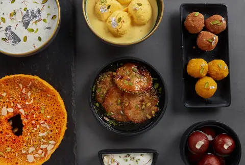 Assorted Indian sweets including gulab jamun and ras malai in bowls