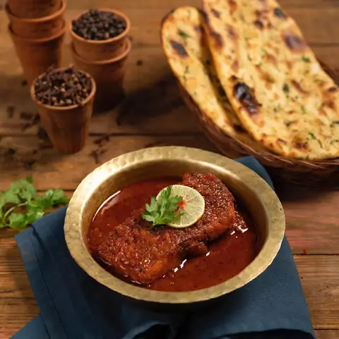 Fish curry garnished with lemon slice and coriander with naan bread