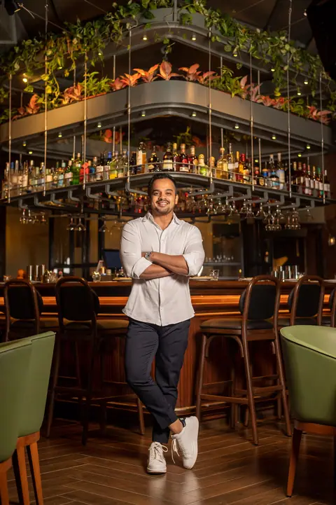 Man standing inside restaurant bar area with hanging bottles and plants