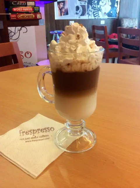 Tall glass of layered coffee topped with whipped cream on a wooden table