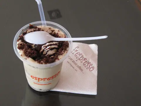Cold coffee topped with chocolate syrup and brownie pieces in a plastic cup