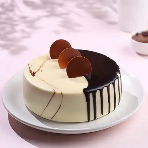 Round cake with white and dark chocolate glaze and chocolate discs on top