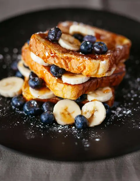 French toast topped with banana slices, blueberries, and syrup on a black plate