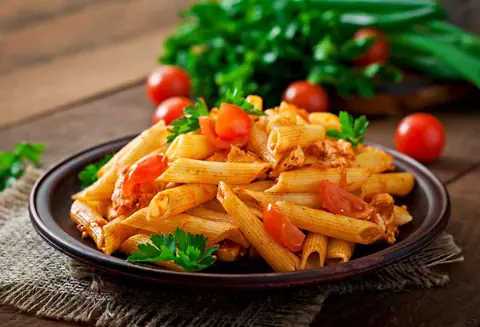 Penne pasta with tomato sauce and herbs on a black plate
