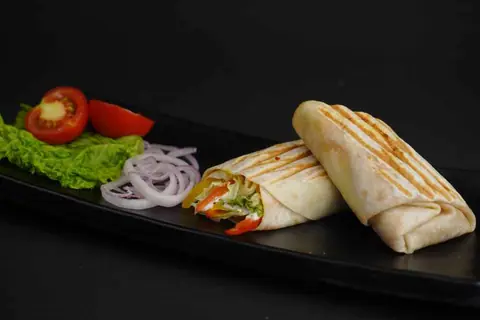 Grilled wrap sandwich with lettuce, tomato, and onions on black plate
