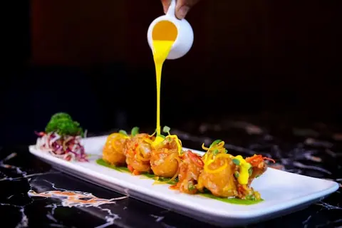 Crispy fried bar snack with yellow sauce being poured on top
