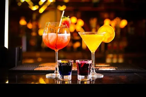 Two cocktails and two shots on a bar counter with blurred lights