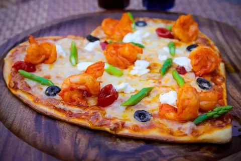 Heart-shaped pizza topped with shrimp, asparagus, olives, and cheese