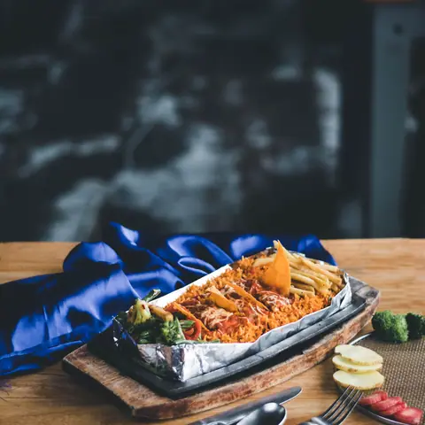 Biryani served in foil with papad and sliced vegetables on wooden board
