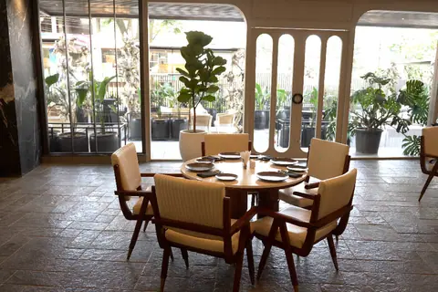 Round dining table with four chairs near large glass doors and plants