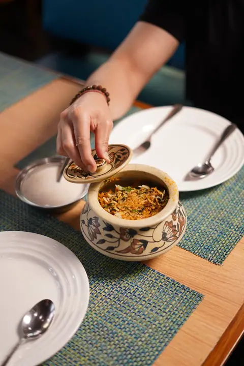 Hand lifting lid from ceramic pot containing biryani rice