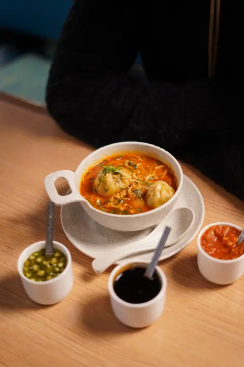 Soup with momos and three different chutneys in small bowls