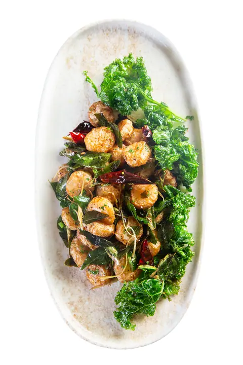 Spiced fried prawns with curry leaves and crispy kale on a white plate