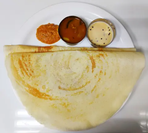 Plain dosa served with red chutney, sambar, and coconut chutney on a white plate