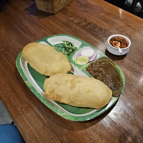 Two kachoris with green chutney, onion slices, lemon, and curry on a plate