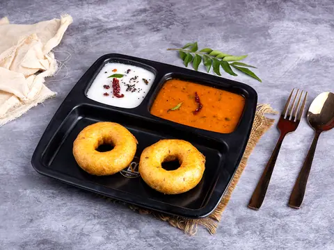 Two medu vadas with sambar and coconut chutney on a black plate