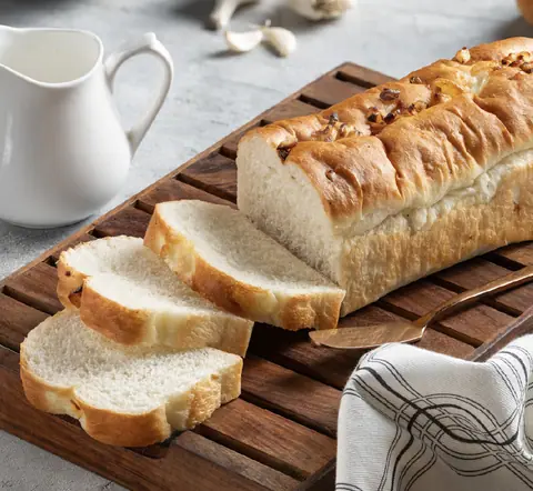 Sliced loaf of white bread with nuts on wooden cutting board