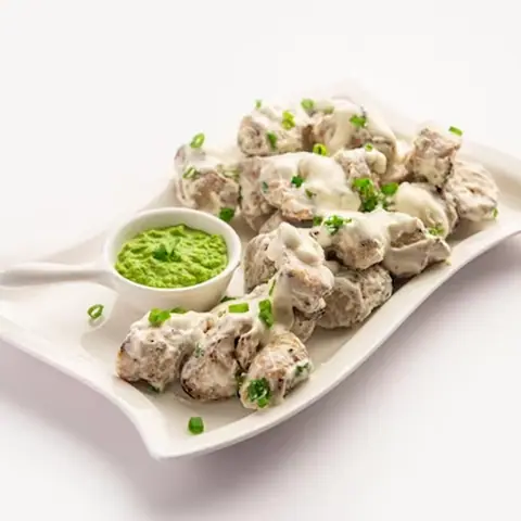 Chicken pieces coated in creamy white sauce with green chutney