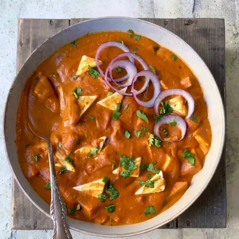 Paneer butter masala garnished with onion rings and coriander in a bowl