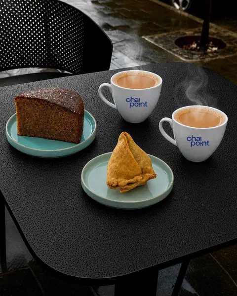 Two cups of chai with a slice of cake and a samosa on plates
