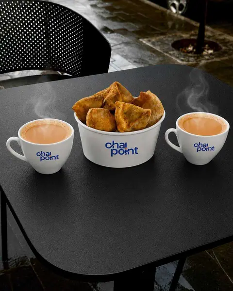 Two cups of chai and a bowl of samosas on a black table