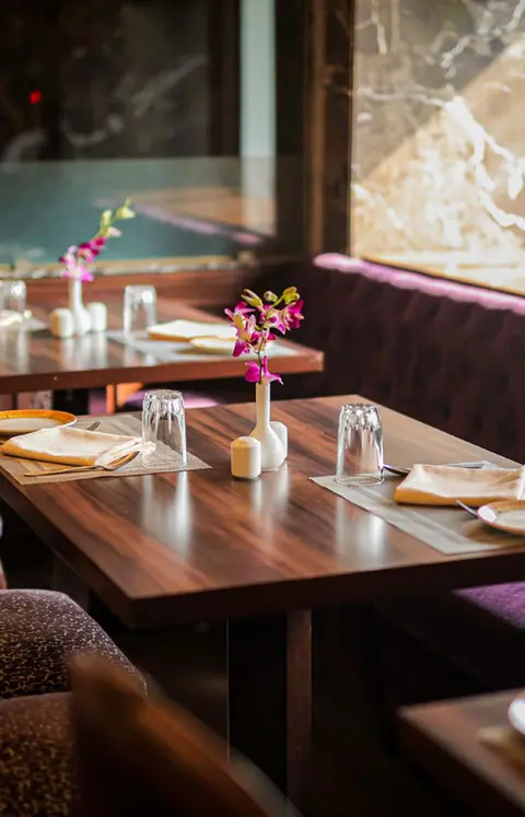 Wooden dining table set with glasses, napkins, and flower vase in restaurant