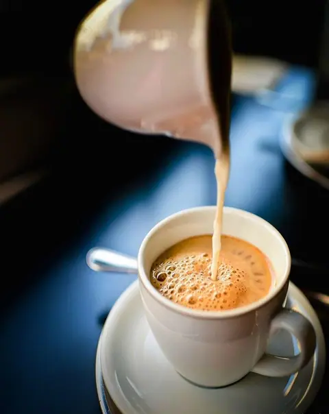 Hot tea being poured into a white cup on a saucer