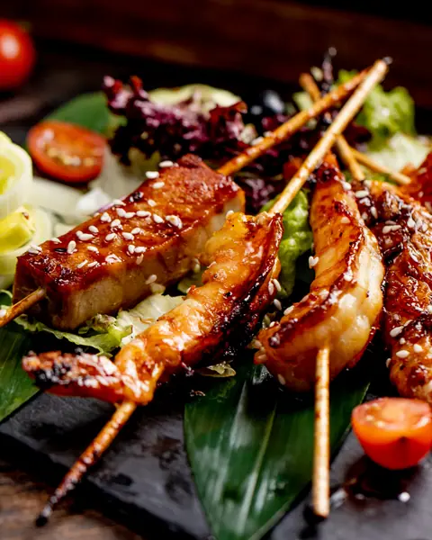 Grilled skewers of meat with sesame seeds and salad garnish