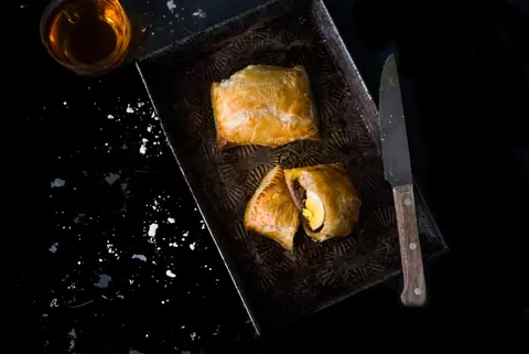 Two pieces of baked pastry with filling on a black tray with a knife