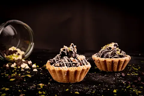 Chocolate tartlets topped with white drizzle and chopped nuts