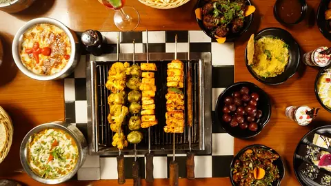 Grilled skewers with various vegetables and side dishes on a checkered table