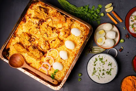 Chicken biryani with boiled eggs and raita in a metal tray