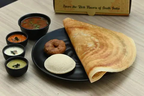Masala dosa with sambar, chutneys, idli, and vada on a black plate