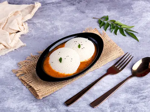 Two soft idlis served with red sambar in a black oval dish