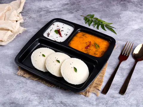 Three idlis with sambar and coconut chutney in a black tray