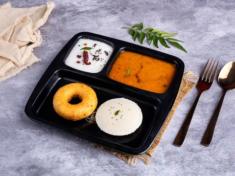 Idli and vada served with sambar and coconut chutney in a black tray
