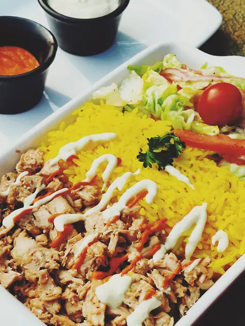 Plate with yellow rice, shredded chicken with white sauce, and side salad