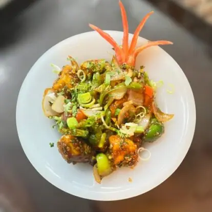 Spicy mixed vegetable dish garnished with chopped spring onions and carrot