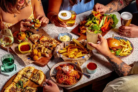 Table with various dishes including pizza, fries, burger, and drinks at a cafe