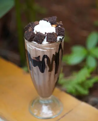 Chocolate milkshake topped with whipped cream and brownie chunks in a glass