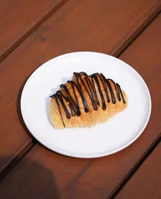 Croissant drizzled with chocolate sauce on a white plate