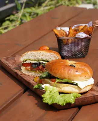 Two sandwiches with lettuce and tomato served with a basket of potato wedges