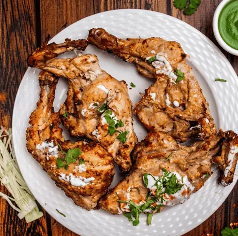 Grilled chicken pieces garnished with herbs and white sauce on a white plate