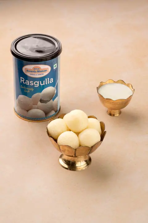 Rasgulla sweets served in traditional brass bowls with a can in background