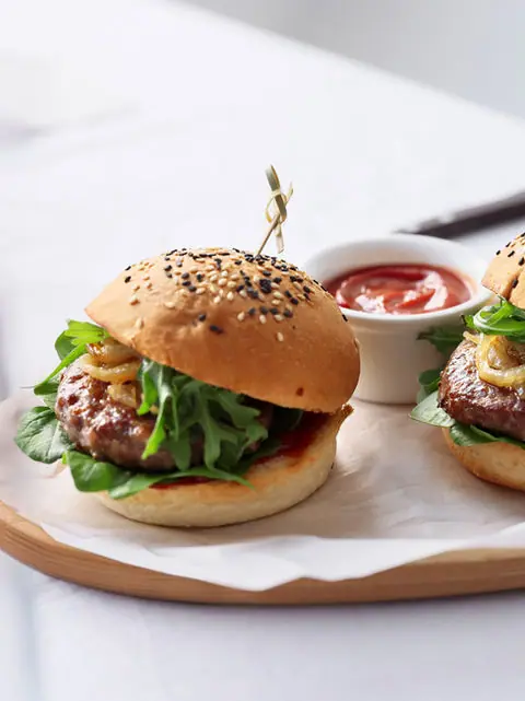 Two burgers with lettuce and onions served with ketchup on a wooden platter