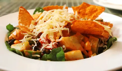 Salad topped with shredded cheese and nacho chips on a white plate