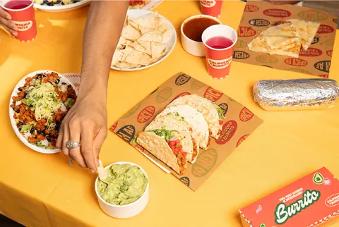 Tacos, burrito, guacamole, and salsa served on a yellow table