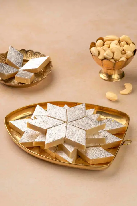 Silver-coated Indian sweets arranged on a brass tray with cashew nuts